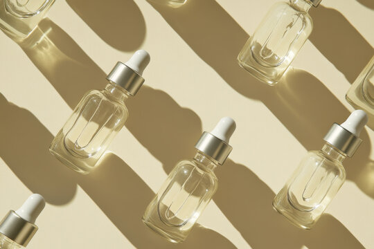 Glass vials with dropper lid in sunlight on beige background. Diagonal flat lay of unmarked containers with cosmetic serum with hard shadows. Close-up, vertical image