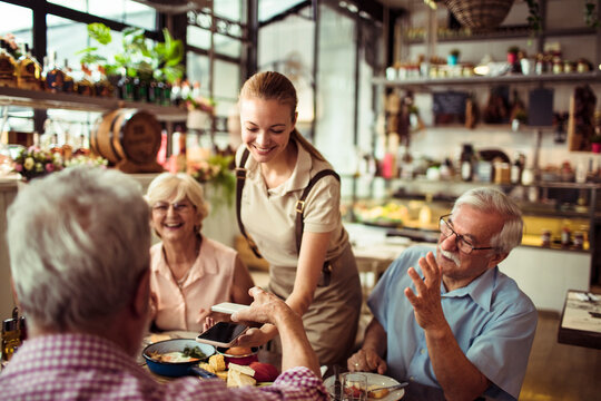 Waitress assisting senior friends with payment at restaurant