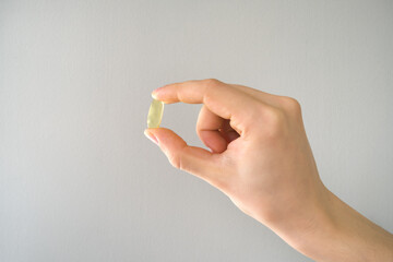 Male hand holding fish oil capsule isolated on grey background. Fish oil capsules, omega 3, omega 9, vitamin D, vitamin E