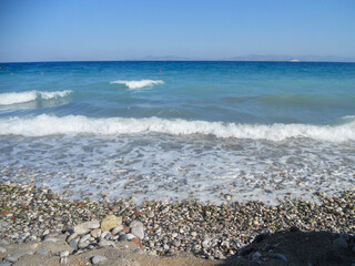 Waves gently lap on a pebbly beach in Greece