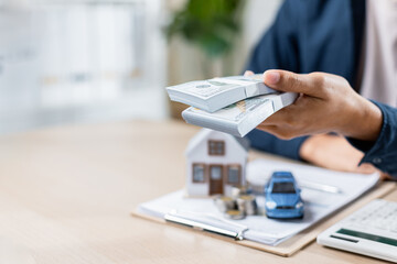 person holding cash over model house and car on table