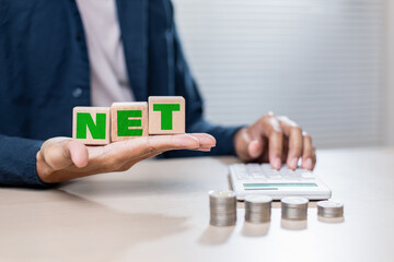 Wooden blocks spelling NET held by person near calculator and coins