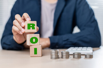 Businessman stacking ROI blocks with coins and calculator