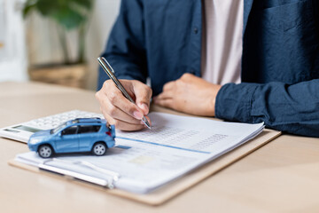 person writing on document with toy car and calculator nearby