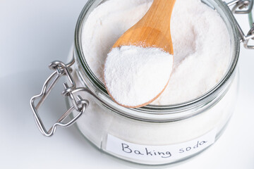 Baking soda in a glass jar with a wooden spoon on a clean countertop for kitchen use and baking. A wooden spoon rests on the jar. DIY cleaning method using natural products to remove stains. top view