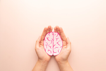 Woman hands holding human brain shape made from paper on beige background. Awareness of Alzheimer, Parkinson's disease, dementia, stroke, seizure or mental health. Neurology and Psychology care.