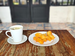 A plate of golden brown banana fritters sits beside a cup of hot lemon.