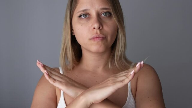 Close up of young woman showing sign of denial, refusal, rejection crossing her arms in front of her on grey background. Girl making gesture by turning her head left and right, giving negative answer