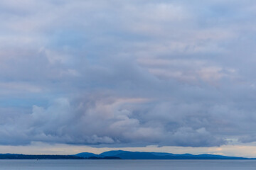 Fototapeta premium Overcast Sky Above Coastal Landscape With Distant Hills and Calm Water