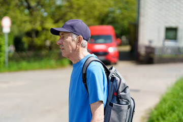 Elderly man with a backpack on his shoulder walking along the street