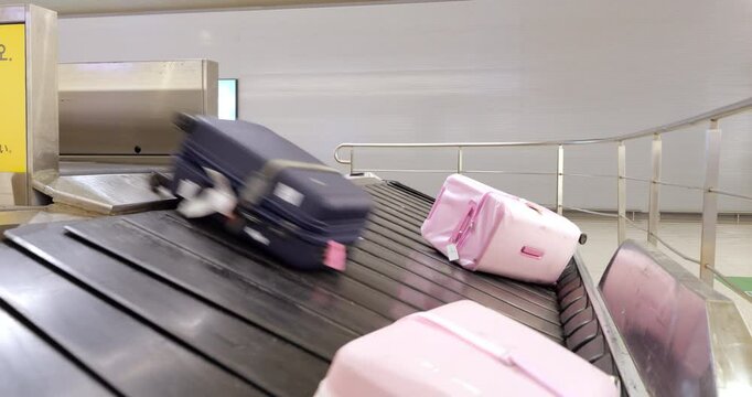 At airport baggage claim area, large pink suitcase rolls down onto the luggage conveyor belt, followed by dark suitcase. Typical arrival scene during baggage claim for an international flight