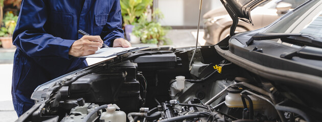 Auto check up and car service shop concept. Mechanic writing job checklist to clipboard to estimate repair quotation to client at workshop garage.