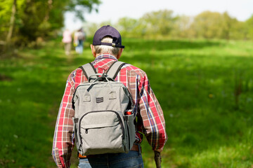 Back view of senior man with walking stick and backpack in the countryside