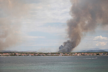 Wildfire burning forest near the Adriatic Sea in Croatia. Flames and smoke rise in the background while calm blue water fills the foreground, showing contrast between nature and disaster.