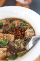Beef noodle soup in a steaming bowl on a dark wooden table, packed with meat and veggies, suitable for lunch or dinner