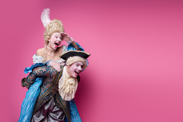 Joyful couple in elegant baroque costumes having fun against a vibrant pink backdrop, embodying historic nobility