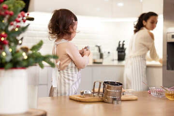 Cute little child girl in apron helping mom bake cookies in the kitchen, Christmas time