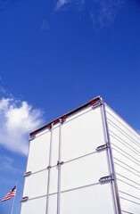 Trailer door with flag, blue sky., and clouds.