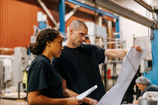 Mature man holding blueprint while standing next to female colleague in warehouse