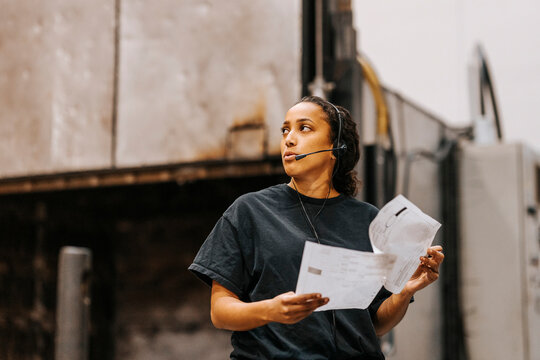 Female worker talking through headset while holding document in warehouse