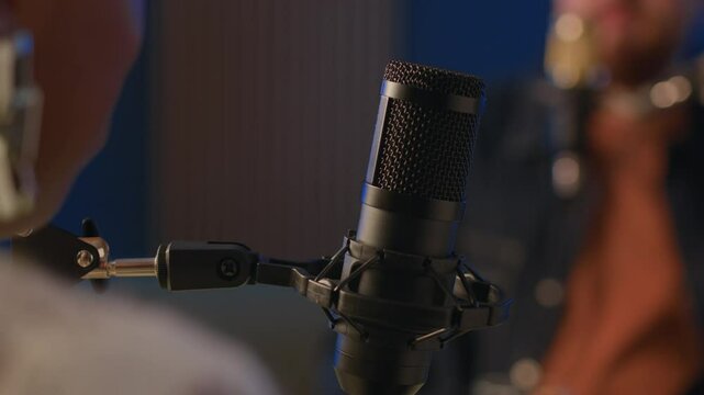 Cropped shot of podcasting process with unrecognizable blurred man and woman engaged in conversation speaking in professional microphone in focus