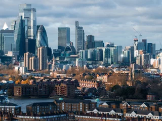 Gordijnen The image captures an aerial view of London's skyline with the Gherkin and modern skyscrapers in Canary Wharf, alongside traditional brick buildings by the Thames. © Aerial Film Studio