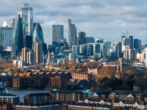 The image captures an aerial view of London's skyline with the Gherkin and modern skyscrapers in Canary Wharf, alongside traditional brick buildings by the Thames.