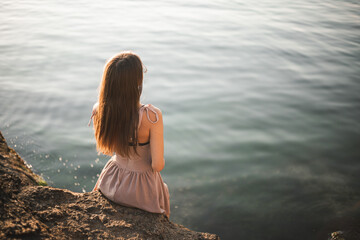 Girl at sunrise on the sea. Silhouette of a slender young girl against the backdrop of the rising sun. Summer, sea, rocks. Vacation at sea. Vacation in warm regions.