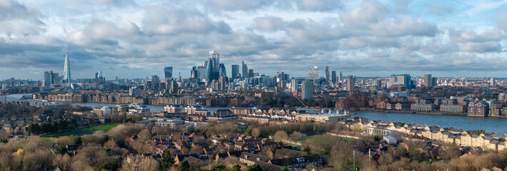 Obraz premium Aerial view of London with The Shard on the left, Canary Wharf's modern buildings, and the River Thames winding through the urban skyline.
