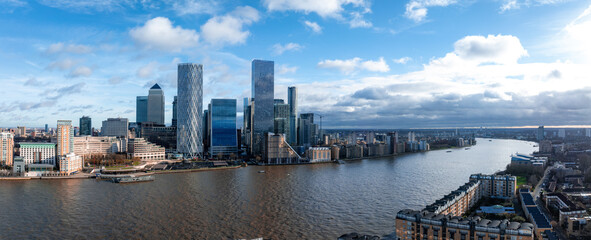 An aerial perspective of Canary Wharf in London, highlighting modern skyscrapers like One Canada Square and the winding River Thames under a partly cloudy sky.