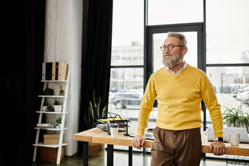 Fototapeta premium A handsome man in a yellow sweater stands confidently in a modern office, looking outside.