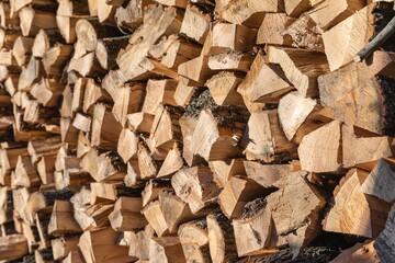 Stacked firewood logs illuminated by sunlight, creating a rustic winter texture