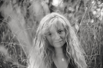 A black-and-white portrait of a woman with Slavic features and straw-colored hair, standing amidst...