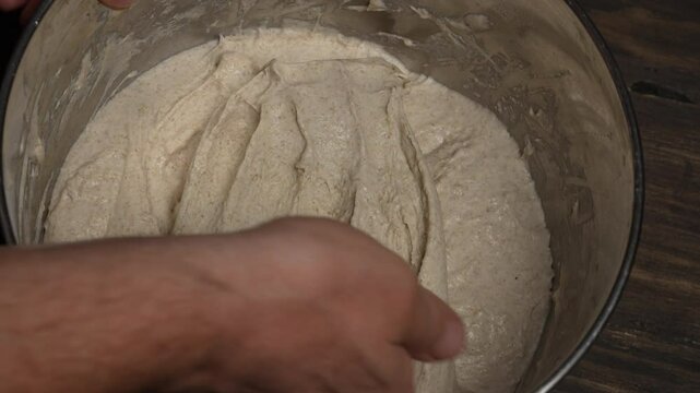 Male baker stretches out yeast-free dough for baking bread with his hands, close up, top view