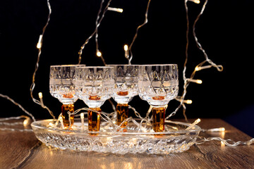 Crystal glasses on a crystal tray with a Christmas tree garland on a dark background.