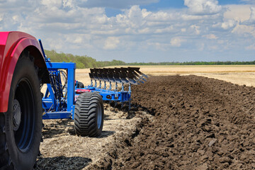 A large red tractor with a plow standing in a field. Start tillage after harvest.