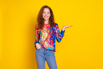 Young woman with curly red hair wearing a colorful trendy print sweatshirt against a yellow background showing a playful and charming smile