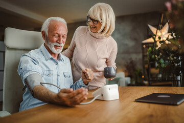 senior wife support and help her senior husband to measure blood pressure