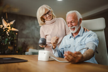 senior wife support and help her senior husband to measure blood pressure