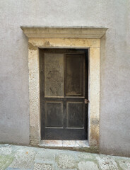 Korcula, Croatia - June 30, 2024: Old blue door closeup set in gray flat cement wall in squre frame on Don Iva Matijace Opate alley