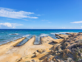 Scenic coastal view with unique rock formations, turquoise sea, and clear blue sky under sunlight.