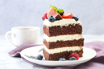 Piece of delicious chocolate sponge cake with berries and tea on white table, closeup
