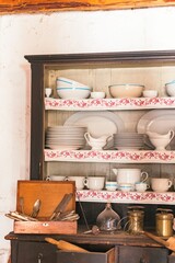 In a cozy kitchen, a wooden cabinet displays an array of vintage dishware, including elegant plates and bowls. The charming arrangement invites nostalgia while highlighting rustic design elements