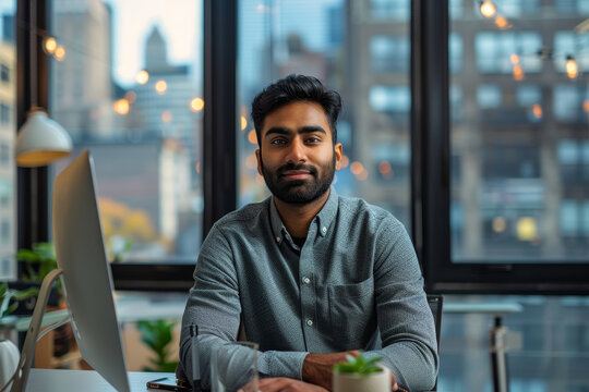 A South Asian tech startup founder delivers a presentation in a sleek open-plan office with a city skyline visible through large windows.