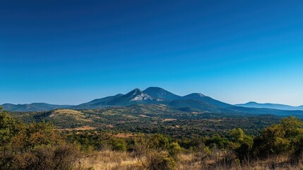 Fototapeta premium Panoramic view of rolling hills and valleys under a clear blue sky in a serene mountain landscape