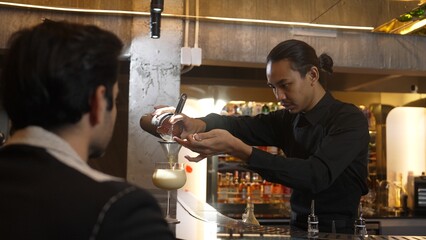 Asian smart bartender shaking mixed cocktail preparing to serve at luxurious counter preparation making special drink serving to customer fronted bar. Special refresh drink nightlife luxury. Vinosity.