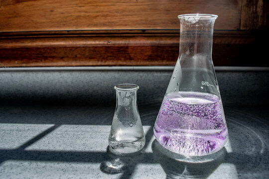 Erlenmeyer flask chemistry laboratory or lab equipment with a purple liquid substance or formula for medical or chemical uses. Transparent glass with wooden and marble background