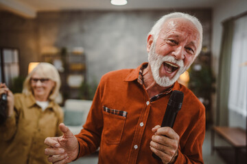 senior man sing karaoke on microphone with senior woman dance behind