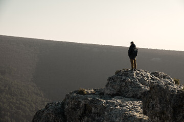 Tourist cliff mountain. Silhouette against the background of bright sunlight. A young man stands on the edge of a cliff. The concept of an active lifestyle. Demonstration of the brown colors of 2025