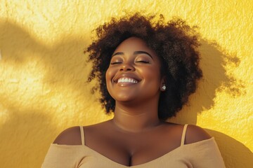 Plus size African American confident smile woman with curly black near yellow wall. Overweight black female in casual clothes in summer. photo